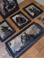 Five framed vintage silhouette pictures and one small rectangular tray depicting romantic or social scenes in black cut-out style on soft muted backgrounds.