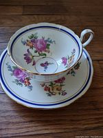 Top angled view of Aynsley Claridge teacup showing floral pattern inside cup, cobalt blue border and gold trim with matching saucer underneath on wooden surface.