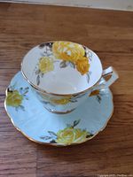 Aynsley teacup and saucer with yellow rose floral pattern, showing top view of cup inside saucer.