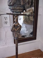 Close-up of top of fireplace utensil stand showing detailed figure of a woman in period dress