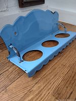 Side angle of the light blue enamel metal jar holder with three circular jar openings on hardwood floor.