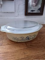 Full view of the Pyrex casserole dish with clear glass lid on wooden surface, showing the beige speckled design and blue Homestead pattern.