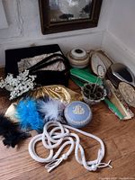 Overview of lot items: beaded tassel belt, feather fascinator, several shuttered bags, vanity jars and mirrors, feather brooches.