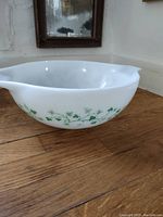 Large white glass mixing bowl with green ivy leaf and vine pattern on the side, placed on wooden table.