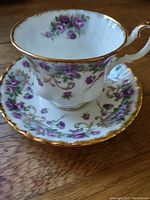 Teacup and saucer set showing purple rose pattern with gold trim on white china base