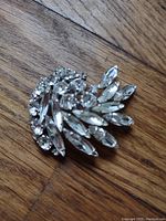 Top view of clear crystal Sherman brooch showing round and marquise shaped stones in silver-tone metal setting laid on wood surface