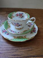 Photo of stacked teacup, saucer, and dessert plate showing floral design, gold details and green sections.