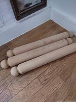 Three large wooden rolling pins lying on a wooden floor, showing full length and handles.