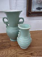 Tall and small green ceramic vases displayed on a wooden surface under a mirror.