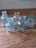 Front view of five aqua glass vintage inkwells and small bottles on wooden floor surface