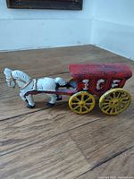 Side view of vintage cast iron ice wagon horse and wagon with red paint and yellow wheels, 'ICE' visible on wagon side.