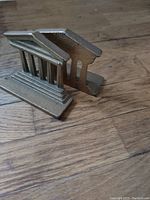 Side view of one brass Greek ruin bookend showing textured finish and slanted top with vertical columns