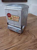 Front and angled view of vintage metal toothpick dispenser showing label and dispensing lever
