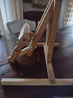 Front and angled side view of the wooden tabletop artist easel on a table, showing the adjustable clamp and hinges.