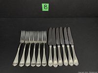 Six forks and six knives arranged on black backdrop