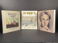 Front cover view of three books: Toronto in Art by Edith G. Firth, Morrice by G. Blair Laing, and Berryman Street Boy by Duval, showing cover art.
