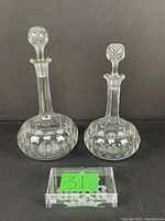 Pair of clear cut glass decanters with rounded bases, long necks, etched decoration, and spherical stoppers, shown from the front with a small acrylic label bearing number 31
