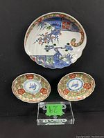 Photo showing two small round Japanese Imari dishes with colorful floral and geometric patterns and one larger oval Imari dish with intricate blue, red, green and gold motifs arranged on a black background.