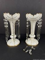 Front view of both opaque milk glass Victorian lustres with attached crystal hanging drops and some detached drops at base.