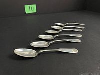 Six sterling silver teaspoons laid out in a line against a black background, showing size and overall appearance.