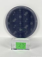 Front view of a smoked glass decorative plate showing the fabric pattern with geometric and abstract shapes against a dark smoky background.