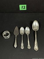 Full lot arranged in a straight line: napkin ring, dessert server, 2 teaspoons, and dinner spoon