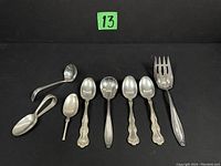 Full view of all eight pieces of sterling silver flatware against black background tagged with number 13