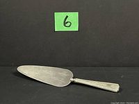 Full view of the sterling silver pie server showing the blade and handle on black background with numbered green label.