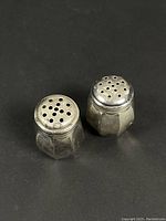 Pair of sterling silver salt and pepper shakers with faceted glass bodies and tarnished silver tops shown front view.