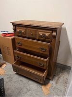 Front angled view of antique wooden four drawer dresser showing open drawers, wood carved details, and different drawer handles.
