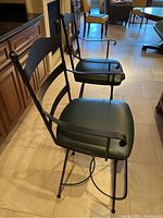 Pair of black wrought iron bar stools with cushioned seats shown side by side from an angled front view.