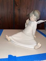 Front angle view of ceramic sitting angel showing details of face, dress, and bare feet