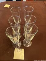Six clear crystal water glasses displayed upright on a brown table with a handwritten note card stating '6 crystal water glasses'.