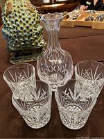 Four crystal highball glasses arranged in a partial circle around one crystal decanter, showcasing cut floral and starburst patterns.