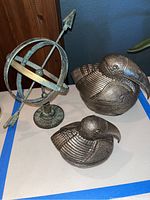 Two silver bird-shaped canisters and decorative pewter globe with arrow on table.