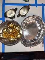 Top-down view of silver serving dish and silver compote dish holding gold pear-shaped ornaments, and Poole silver sugar pitcher and creamer.