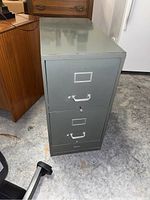 Two-drawer gray metal filing cabinet viewed from front, showing drawer handles and label holders.