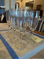 Front angle photo showing the two types of clear glass champagne flutes arranged on a table with 2 of one style and 8 of the other.