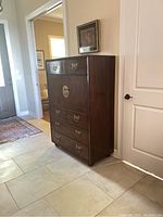 Front and side view of a dark wood highboy chest measuring about 39x57.5x19 inches with brass or pewter handles, placed in a room with tiled flooring.