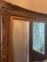 Close-up photo showing the ornate gold carved frame with intricate floral and scroll details.