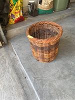 Round wicker basket on concrete floor next to garden supplies, showing overall condition and size.