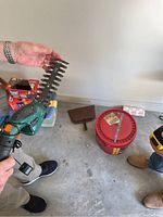Photo showing hands holding the green and black battery operated hedge trimmer with visible blade and orange trigger.