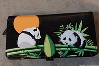 Front of black hand purse showing panda artwork with bamboo and sun design.