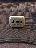 Close-up of the metal plate on the suitcase front with the 'Authentic Jeep Est. 1941' branding.