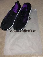 Pair of black and purple Comfort Wear orthopedic shoes on branded translucent storage bag, showing profile angle.