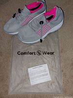 Pair of grey and pink Comfort Wear shoes on top of branded dust bag with informational insert.