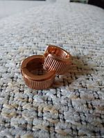 Close-up image of small copper hoop earrings with ribbed texture placed on a gray and beige textured surface
