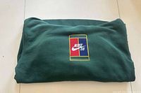 Folded dark green Nike SB pullover hoodie showing front chest logo patch with red, navy, and yellow colors.