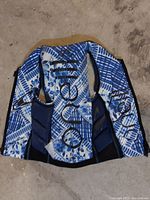 Front view of a blue and white patterned O'Neill life jacket laid flat on concrete floor.