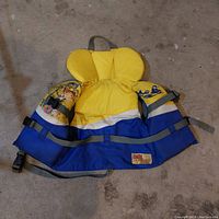 Yellow and blue life jacket with character print, designed for children, with adjustable straps and buckles.